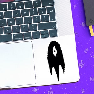 Puede incluir: Una pegatina en blanco y negro de una figura de fantasma estilizada con un solo ojo en una computadora portátil plateada.