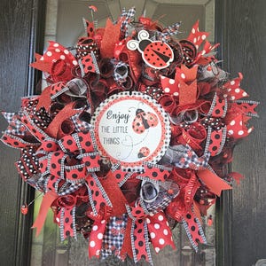 May include: A red, black, and white ladybug themed wreath with a sign that reads "Enjoy the little things".