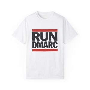 Puede incluir: Camiseta blanca con un gráfico negro y rojo que dice "RUN DMARC" en una fuente en negrita.