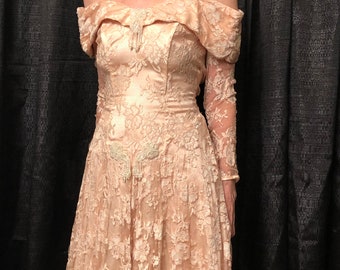 May include: A blush pink off-the-shoulder lace dress with long sleeves and a flowing skirt. The dress features delicate floral embroidery and beaded embellishments.