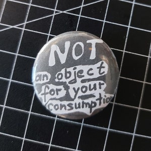 May include: A black and white button with the text "NOT an object for your consumption" written in white.
