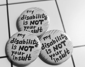 May include: Three white button badges with black text that reads "my disability is NOT your insult".