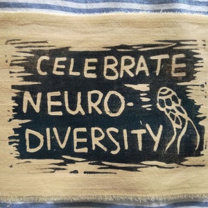 May include: A beige fabric patch with black text that reads "Celebrate Neuro-Diversity" and a black and white illustration of a brain.