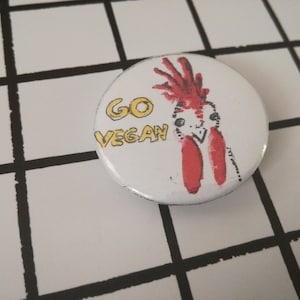 以下が含まれることがあります： 赤い鶏と「GO VEGAN」という文字が描かれた白いボタンです。