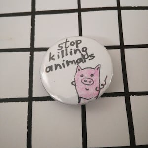 May include: White button with black text that reads "stop killing animals". A pink pig with a black outline is drawn on the button.
