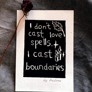 Puede incluir: Una tarjeta blanca con un rectángulo negro con el texto "I don't cast love spells. I cast boundaries." Una rosa seca y su tallo están a la izquierda. La tarjeta está firmada "Lex Kartane".