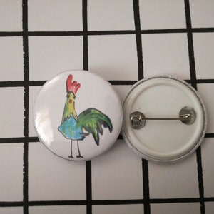 May include: A white button with a colorful cartoon rooster illustration. The back of the button has a metal pin.