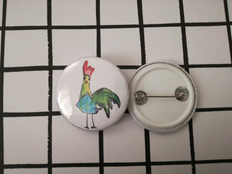 May include: A white button with a colorful cartoon rooster illustration. The back of the button has a metal pin.