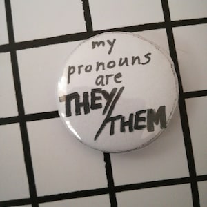 May include: White button with black text that reads "my pronouns are they/them".