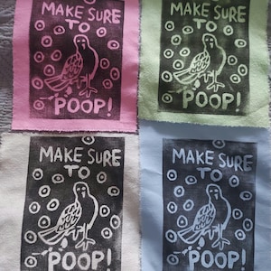 Könnte beinhalten: Vier Stoffquadrate mit einem schwarz-weißen Druck eines Vogels mit dem Text "Make sure to poop!" auf jedem Quadrat. Die Quadrate sind rosa, grün, weiß und blau.