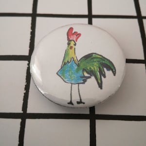 May include: A white button with a colorful cartoon rooster illustration. The rooster is green, blue, and yellow with a red comb.