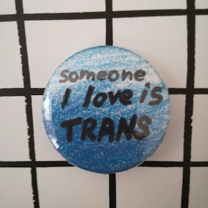 以下が含まれることがあります： 黒文字で「Someone I love is TRANS」と書かれた青と白のボタン