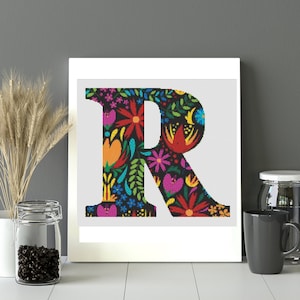 May include: A white frame with a black letter R surrounded by colorful flowers and leaves. The letter is on a white background.