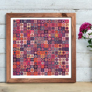 May include: A framed print with a colourful geometric pattern in shades of purple, orange, and pink. The wooden frame sits on a wooden surface next to a vase wrapped in twine, holding pink and white flowers.