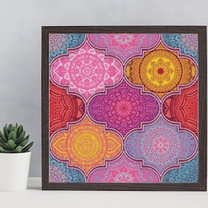 May include: A framed print with a colorful geometric pattern. The design features a variety of pink, red, yellow, and blue mandala-like shapes.