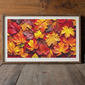 May include: A rectangular framed print featuring a dense arrangement of fallen maple leaves in vibrant shades of red, orange, and yellow. The frame is made of medium-toned wood, and the artwork is displayed with a clean white mat border.