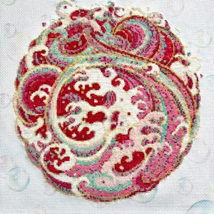 May include: A close-up of a cross-stitch embroidery design featuring a pink, red, and green paisley pattern on a white background.