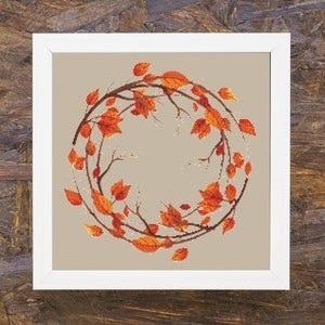 May include: A framed cross-stitch embroidery featuring a wreath of orange and red autumn leaves.