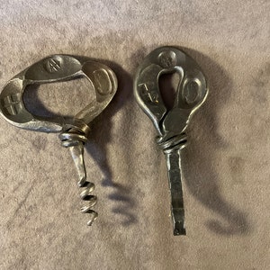 May include: Two metal bottle openers with a unique design. One opener has a corkscrew and the other has a flat blade.