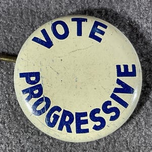 May include: A vintage political button with the words "VOTE PROGRESSIVE" in blue lettering on an off-white background. The button has a pin on the back for attachment.