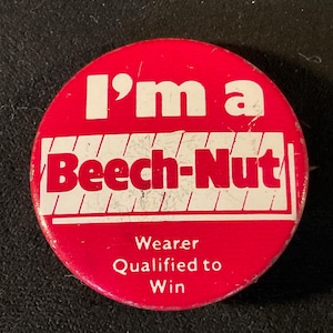 May include: A round, red Beech-Nut button with white text. The button reads "I'm a Beech-Nut" in large letters, with "Wearer Qualified to Win" below. The button is a vintage promotional item.