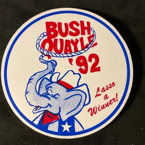 May include: A white round sticker with a blue border. The sticker features a cartoon elephant wearing a cowboy hat and lassoing a rope that says "Bush Quayle '92". The text "Lasso a Winner!" is written below the elephant.