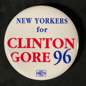 May include: A white campaign button with blue text that reads "NEW YORKERS for CLINTON GORE 96". The words "CLINTON GORE" are in red. A small blue and white union logo is at the bottom.