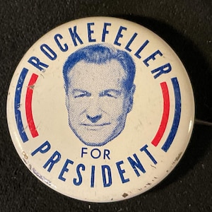 May include: A vintage white campaign button with the text "ROCKEFELLER FOR PRESIDENT" in blue lettering. The button features a portrait of a man in a blue circle, with red and blue stripes. A pin is attached to the back.