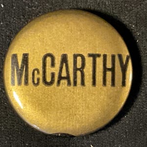 May include: A gold-colored button with the word "McCarthy" printed in black.