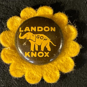 May include: A yellow felt flower pin with a brown button featuring a cartoon elephant with the text "LANDON GOP KNOX" in yellow.