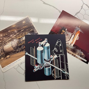 May include: Three vintage space shuttle prints. One shows the Space Shuttle External Tank, another depicts the shuttle launch, and the third features a diagram with the text "Aboard the Space Shuttle". The prints are on a white marble surface.