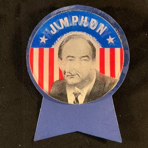 May include: A vintage campaign button featuring a portrait of a man, with the name "JIM PHON" in blue lettering. The button has a red and white striped background and blue accents, with a star on each side of the name.