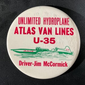 May include: A white, circular button featuring red text that reads "UNLIMITED HYDROPLANE ATLAS VAN LINES U-35." A green hydroplane illustration is below the text, with "Driver-Jim McCormick" in red. The hydroplane is labeled "U-35".