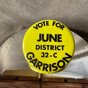May include: Yellow button with black text that reads "Vote for June District 32-C Garrison".