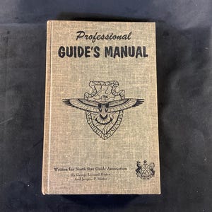 May include: A tan-colored book titled "Professional GUIDE'S MANUAL" with a graphic of an eagle and shield. The book is written for the North Star Guide Association by George Leonard Henter and Jacques P. Hester.