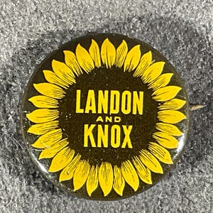 May include: A round pinback button featuring a dark brown center with the yellow text LANDON AND KNOX printed in the middle. The text is surrounded by a border of yellow sunflower petals radiating outward against the dark brown background.