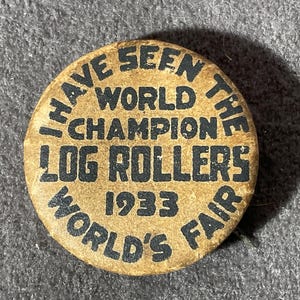 May include: Vintage button with text: "I HAVE SEEN THE WORLD CHAMPION LOG ROLLERS 1933 WORLD'S FAIR." The button is circular, with a tan background and black lettering. A collectible item.
