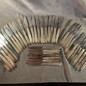 May include: A set of 35 silver-plated dinner knives. The knives are arranged in a semi-circle with the handles facing up. The knives have a simple design with a slightly curved blade and a rounded handle.