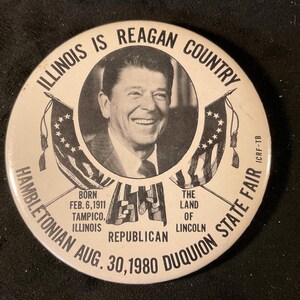 May include: A vintage button with a portrait of Ronald Reagan, labeled "Illinois is Reagan Country." The button includes text about his birth in Tampico, Illinois, and the 1980 DuQuoin State Fair.