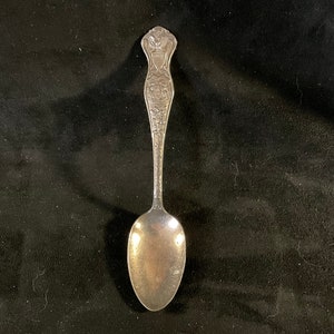 May include: A silver teaspoon with an ornate handle featuring a crown and floral designs.