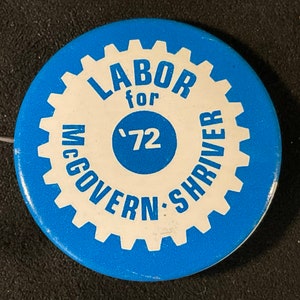 May include: A blue and white button with a gear design. The text on the button reads "Labor for McGovern-Shriver '72".