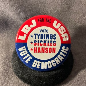 May include: A red, white, and blue political campaign button with the text "LBJ for the USA Vote Democratic" and "vote Tydings Sickles Hanson" in a circle.