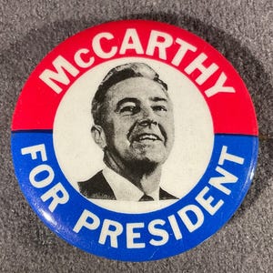 May include: A vintage campaign button with a portrait of a man in a suit. The button has a red and blue border with the words "McCarthy" and "For President" in white lettering. The man's portrait is in the center.