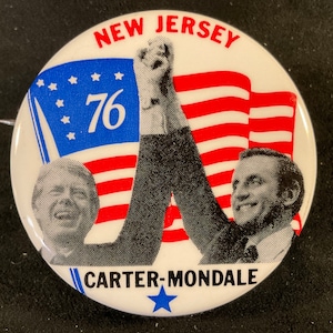 May include: A white button with a red, white, and blue American flag design. The button features the text "NEW JERSEY 76" and "CARTER-MONDALE" with a blue star below. The button also features a black and white image of two men, one with his arm raised in the air.