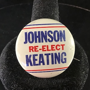May include: A white button with blue and red stripes around the edge. The button says "Johnson Re-Elect Keating" in blue and red letters.