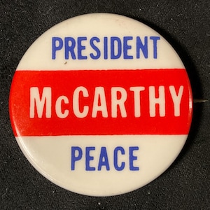 May include: A white button with a red, white, and blue design. The button reads "President McCarthy Peace".