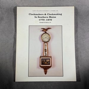 May include: A printed page with the title "Clockmakers & Clockmaking In Southern Maine 1770-1870". The page features an image of a longcase clock with a detailed face, decorative elements, and a small painting at the bottom. An eagle tops the clock.