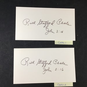 May include: Two white cards with black ink handwriting. The text on the cards reads "Ruth Stafford Beale John 3:16". The bottom of each card has a yellow sticky note with the text "Card 1" and "Card 2" respectively.