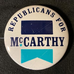 May include: A white button with blue text that reads "Republicans for McCarthy". The button has a blue rectangle and a teal blue chevron shape.