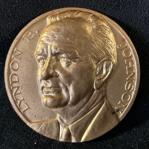 May include: A gold-colored medal with a profile portrait of Lyndon B. Johnson. The medal is inscribed "LYNDON B. JOHNSON" around the edge.